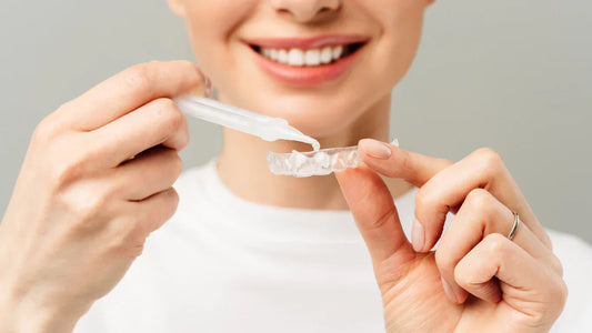 Femeie aplicând gel de albire pe o gutieră dentară pentru albirea dinților.